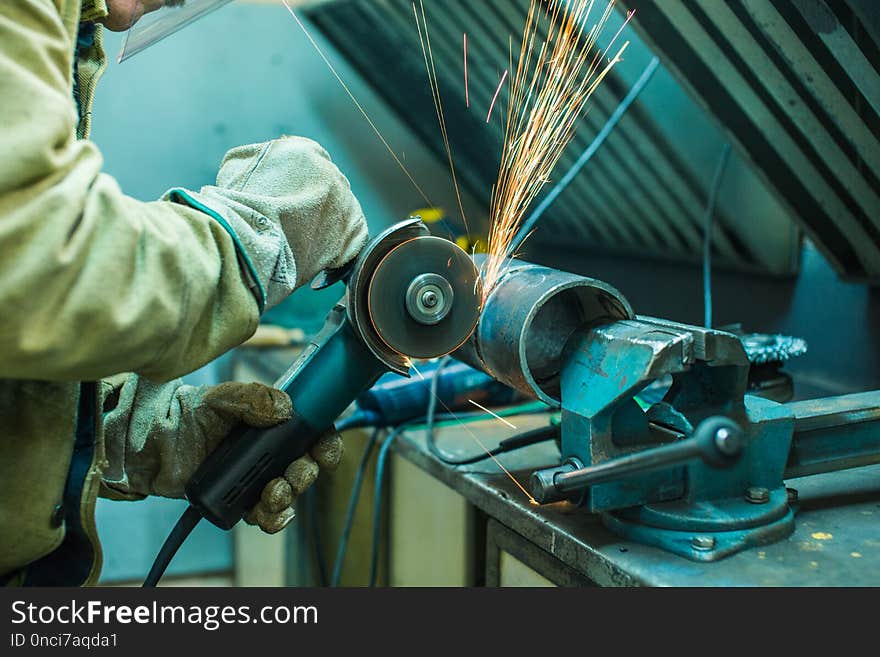 Mechanic cleans a welded seam on a section of a steel pipe with the help of a grinding machine in the metal workshop