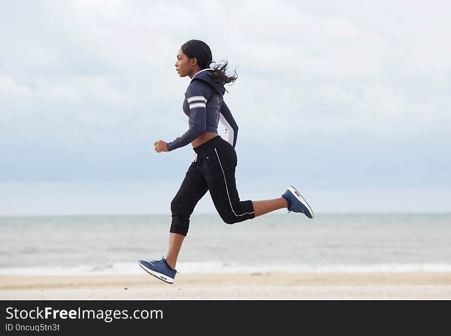 Full body side portrait of sporty young black woman running by the beach. Full body side portrait of sporty young black woman running by the beach
