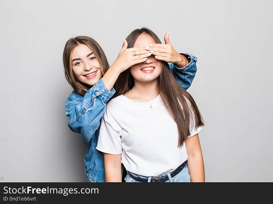 Portrait of two ladies friends looking camera covering eyes with hands standing isolated over gray background