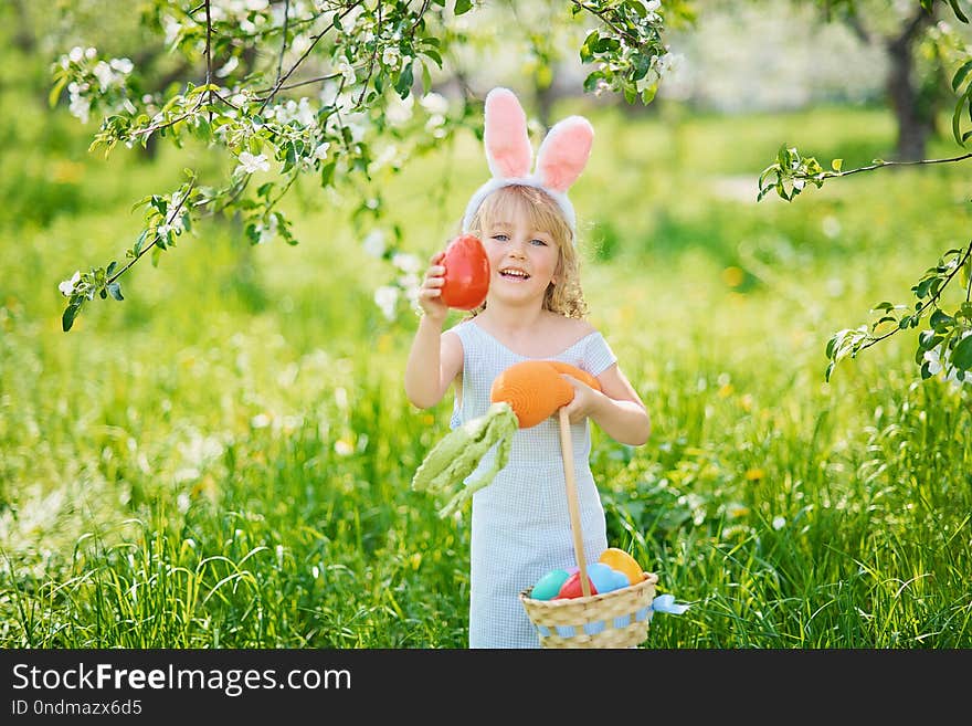 Cute funny girl with Easter eggs and bunny ears at garden. easter concept. Laughing child at Easter egg hunt. Child in park with basket full of eggs, spring concept