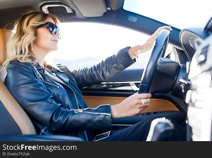 Photo of side of young blonde in black glasses sitting in car during day. Photo of side of young blonde in black glasses sitting in car during day