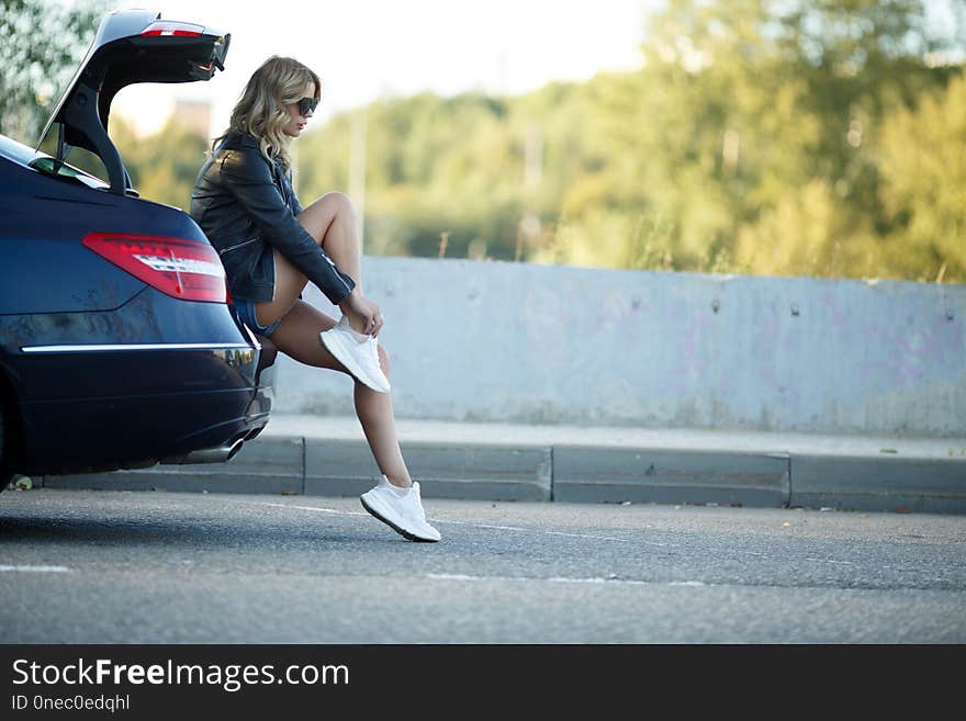 Photo of young woman sitting on broken car with open hood