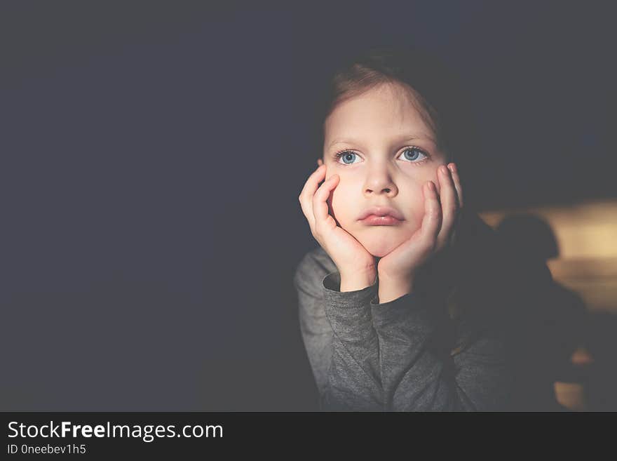 Little sad girl sitting and propping her head with her hands