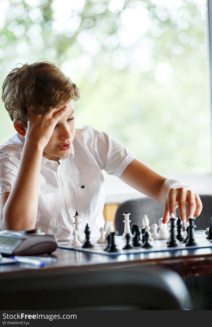 Cute handsome boy in white t shirt plays chess with his rival in chess class. Education concept, intellectual game. Chess tournament, lesson, camp, training concept ,