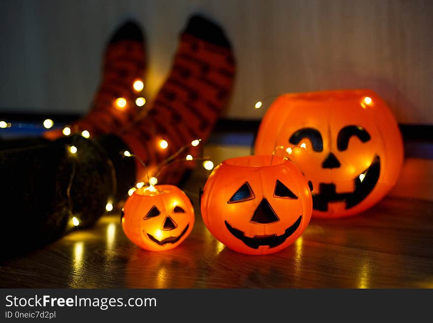 Kids legs in stylish warm bright colorful striped funny socks in garland lights on floor with pumpkins in room. decor for Halloween, cosy moment. cozy autumn days. Happy Halloween celebration concept