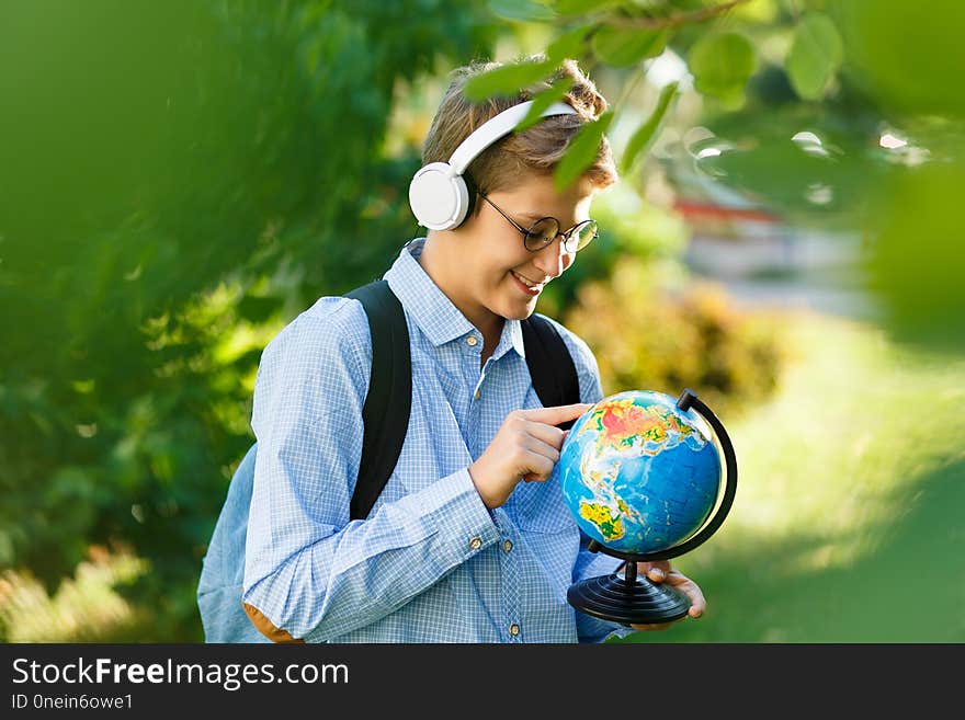 Young boy in blue shirt and round glasses looks and points on globe in his hands. Education, back to school