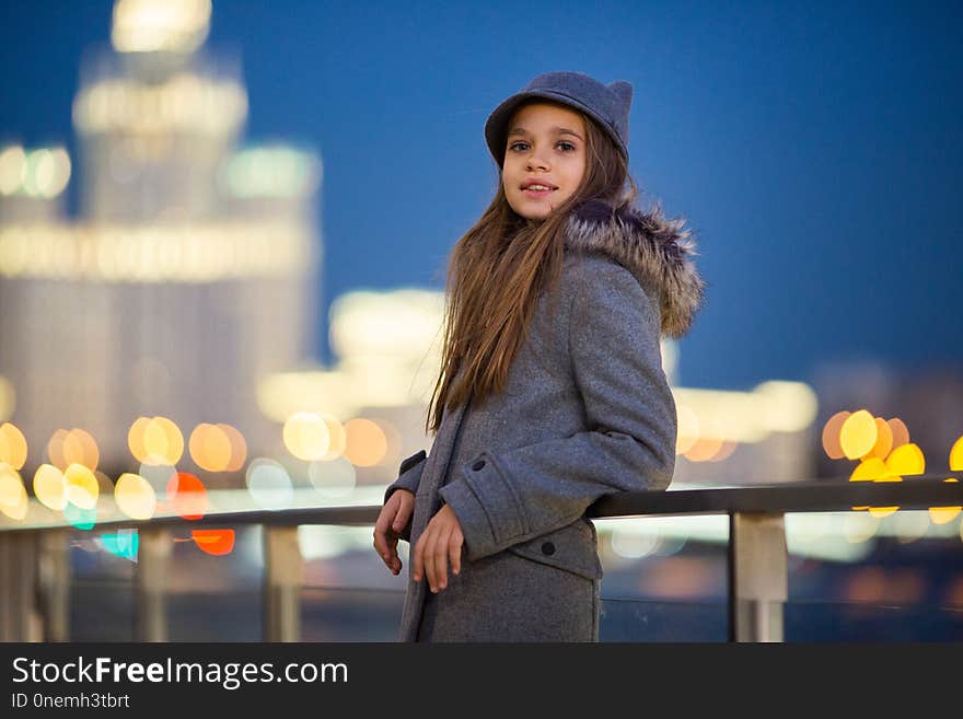 Photo of girl in gray hat and coat on waterfront on background of spots, lights, blurred background