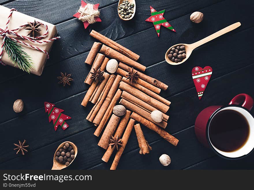 Christmas tree made of cinnamon, star anise, spices and nutmeg with decorations on dark background. Top view