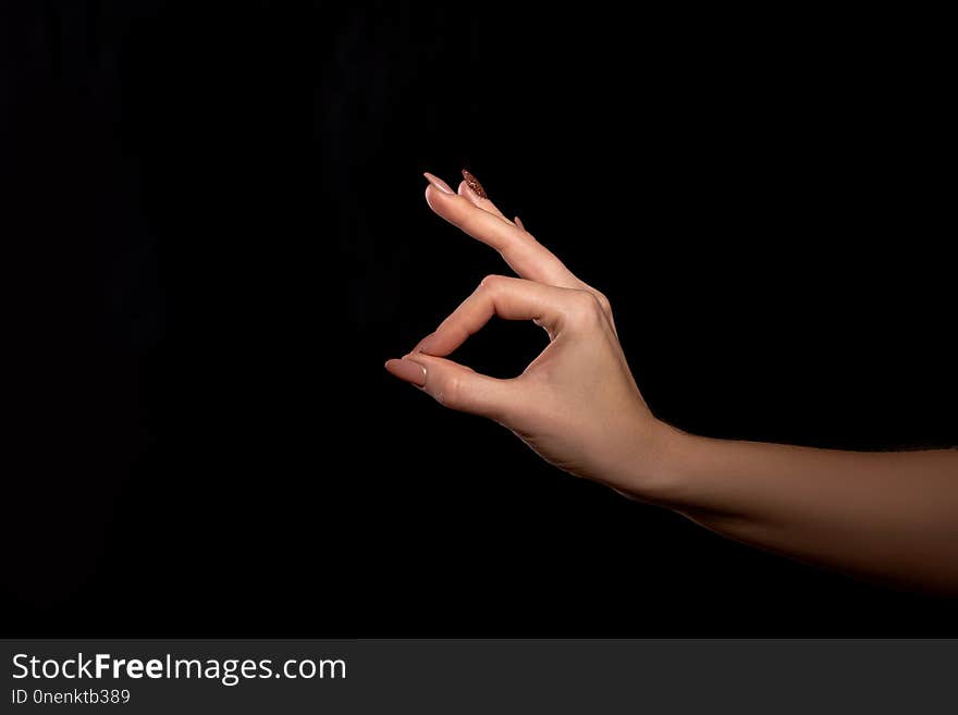 Studio shot of an unidentified woman`s hand showing a gesture of fingers that everything is fine or OK against a black background