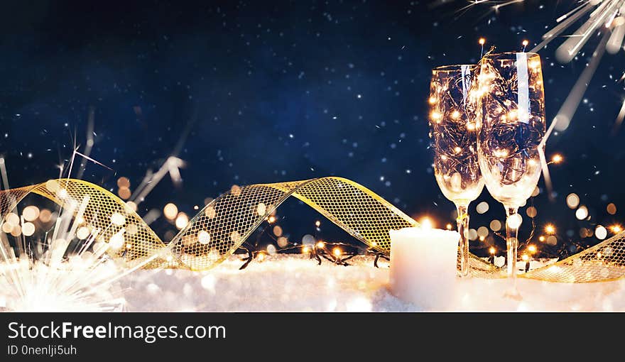 Two glasses filled with garlands with a candle and a gold ribbon in the snow. Christmas card