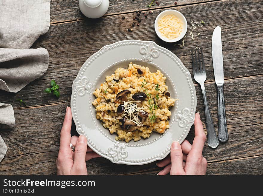 Barley mushrom risotto on plate over rustic wooden background with person holding a plate and vintage cutlery silverware table serving. Top view