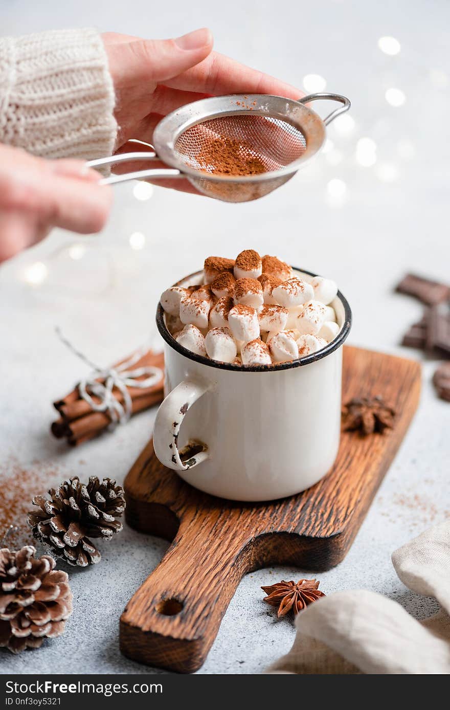 Hot chocolate with marshmallows in mug. Sifting cocoa powder over hot chocolate drink with marshmallows