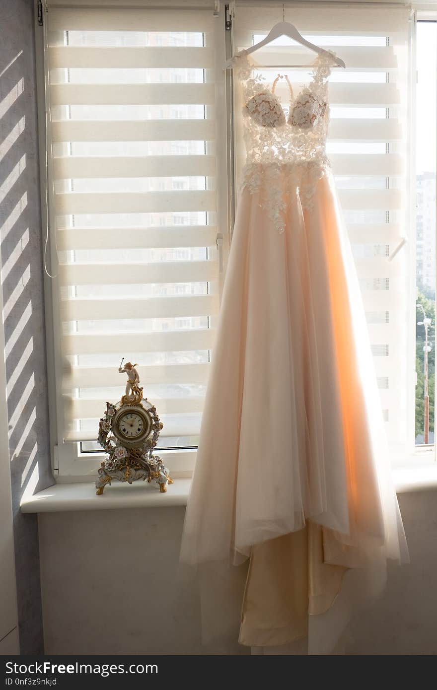 Bright beige wedding dress hanging on a hanger near a window. Bright beige wedding dress hanging on a hanger near a window