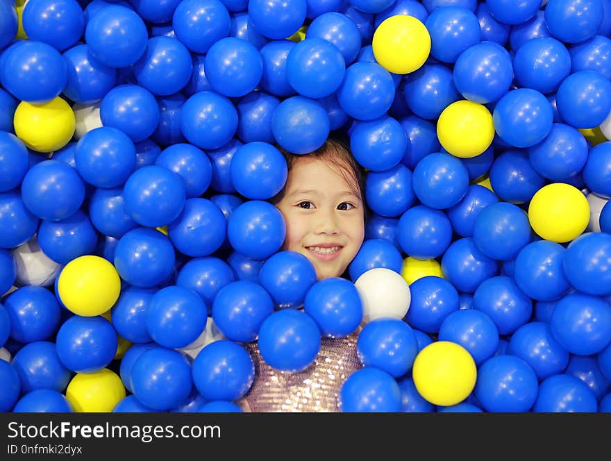 Smiling little girl playing with color plastic balls playground