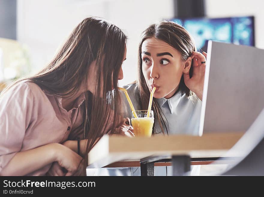 Two beautiful twin girls spend time drinking juice. Sisters relaxing in a cafe and having fun together.