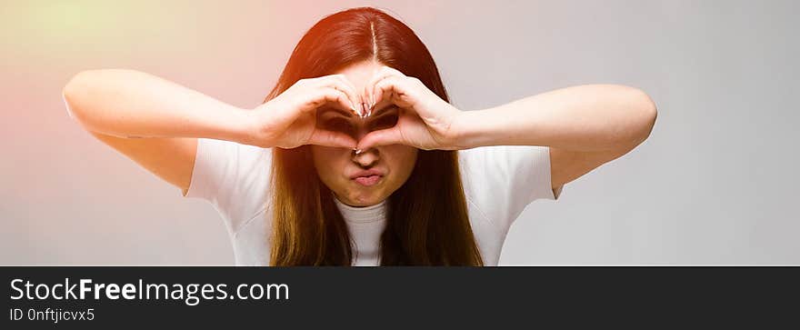 Portrait of plus size model with long hair wearing white blank T-shirt looking through hands making binoculars isolated on grey background with copyspace. Portrait of plus size model with long hair wearing white blank T-shirt looking through hands making binoculars isolated on grey background with copyspace.