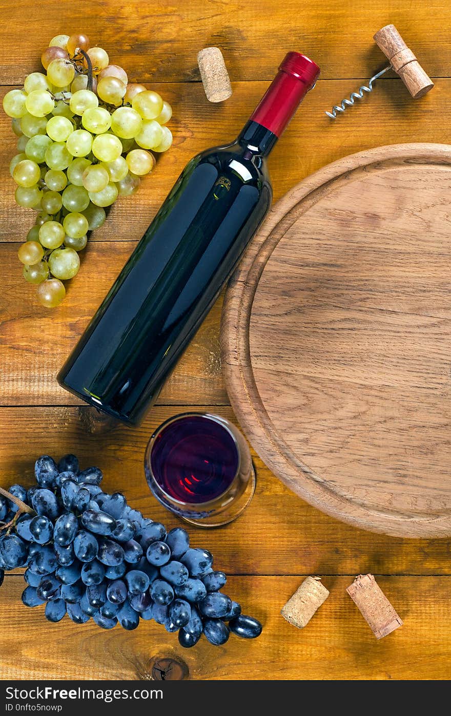 Bottle and glass with red wine, bunches of blue and green grapes, cork and corkscrew on wooden background. Top view, copy-space, flat lay. Bottle and glass with red wine, bunches of blue and green grapes, cork and corkscrew on wooden background. Top view, copy-space, flat lay