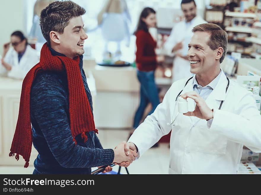 Smiling Pharmacist Handshaking with Customer. Pharmacist Showing a Bottle with Pills to Client. Other Pharmacists and Female Customer on Background. Pharmacists in Medical Uniform. People in Pharmacy.