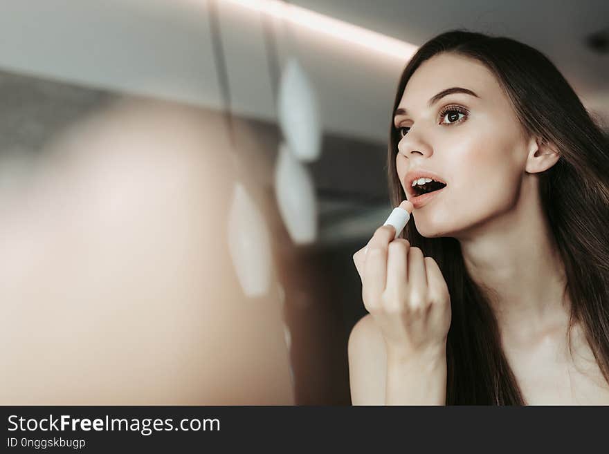 Low angle portrait of concentrated lady rouging lips indoor. Copy space. Natural beauty concept. Low angle portrait of concentrated lady rouging lips indoor. Copy space. Natural beauty concept