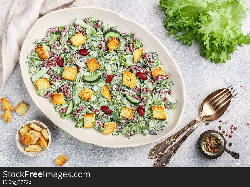 Delicious healthy salad of kidney beans, lettuce, cucumber with bread croutons and yogurt sauce in a white plate. Light gourmet dinner. Selective focus