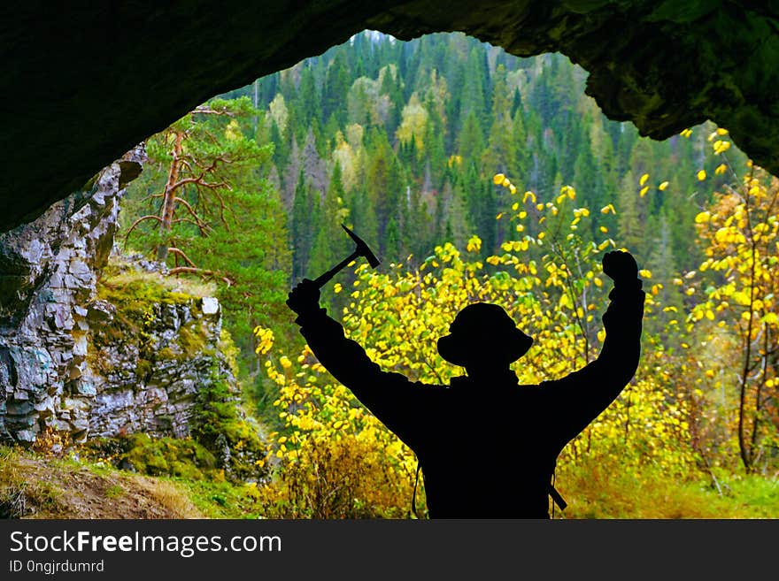 Researcher with a geological hammer in his hand rejoices upon discovering the cave against the backdrop of the autumn mountain landscape outside. Researcher with a geological hammer in his hand rejoices upon discovering the cave against the backdrop of the autumn mountain landscape outside