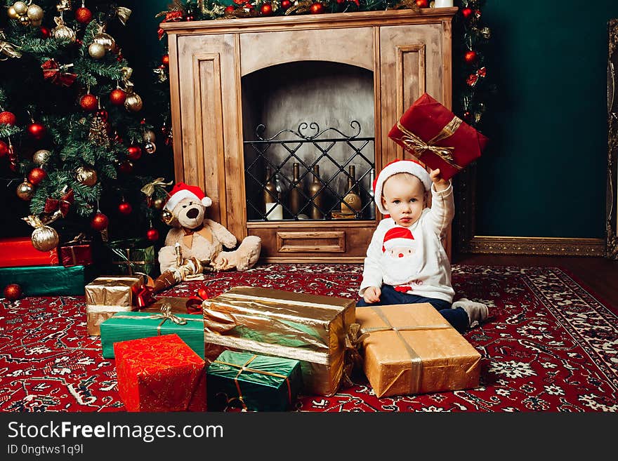 Little Santa boy playing with gifts in decorated studio near fireplace.