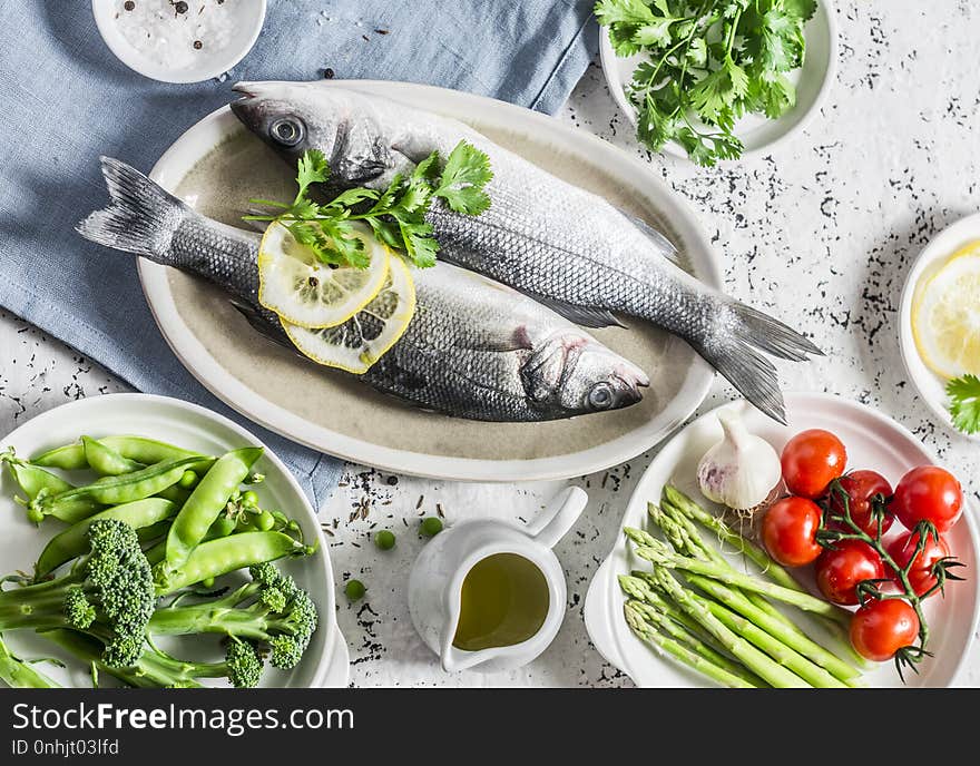 Healthy balanced ingredients for lunch - sea bass, asparagus, tomatoes, broccoli, green peas, olive oil and spices. On a light background, top view. Flat lay