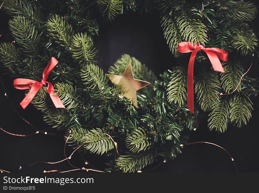Blured dark New Year`s background fir-tree wreath with red ribbon tapes and a gold star
