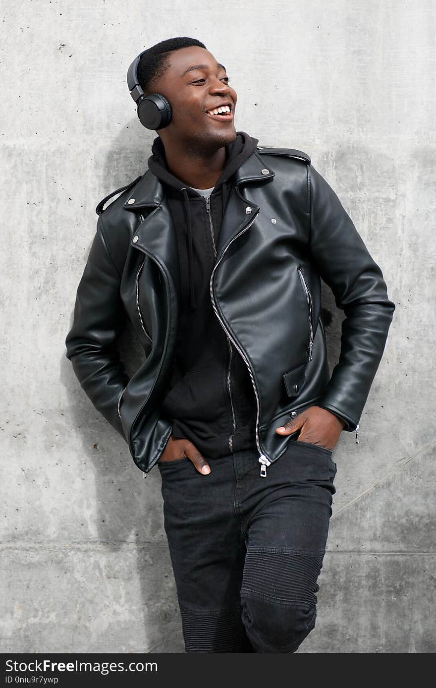 Smiling black man in leather jacket listening to music with headphones