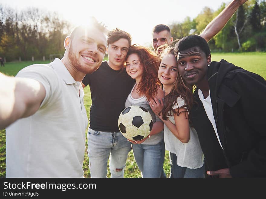 A group of friends in casual outfit do sephi on the soccer field. People have fun and have fun. Active rest and scenic sunset.