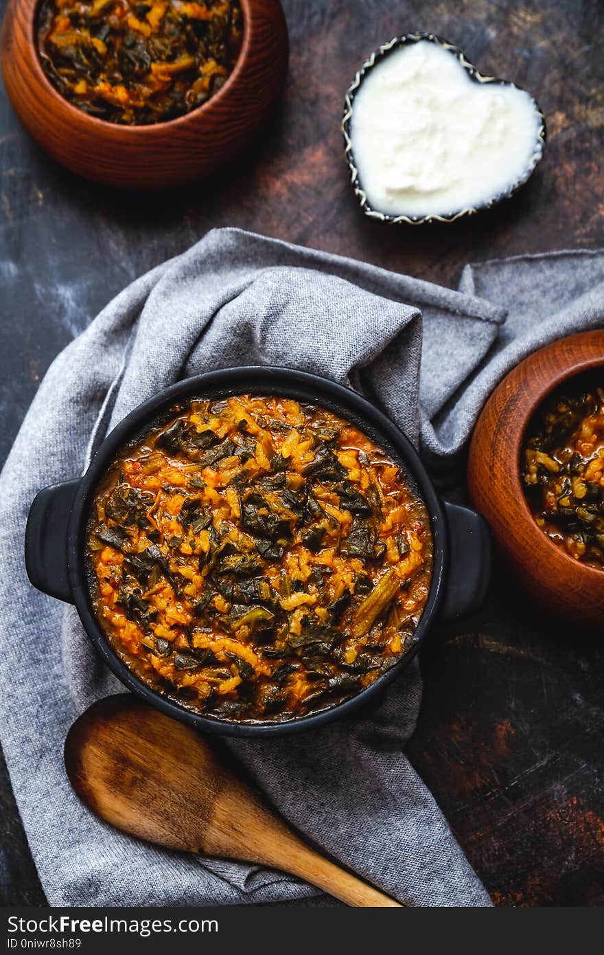 Spinach stew with rice in black pot on dark background