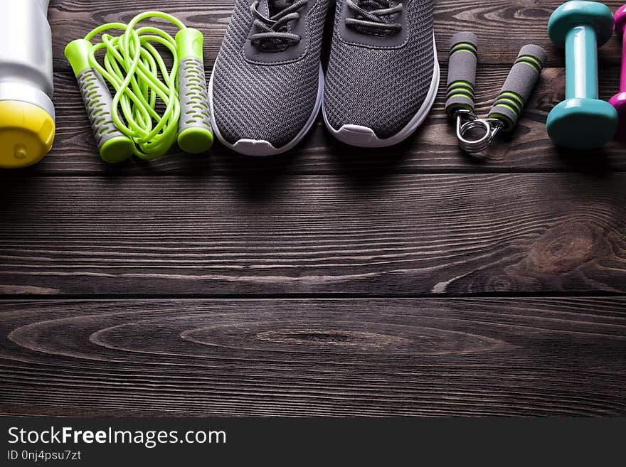 Fitness equipment - water, jumping rope, sneakers and dumbbell on wooden board