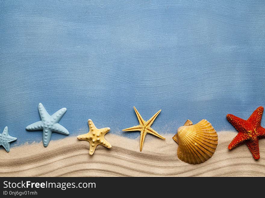 Summertime background - beach sand and seashells on blue table background