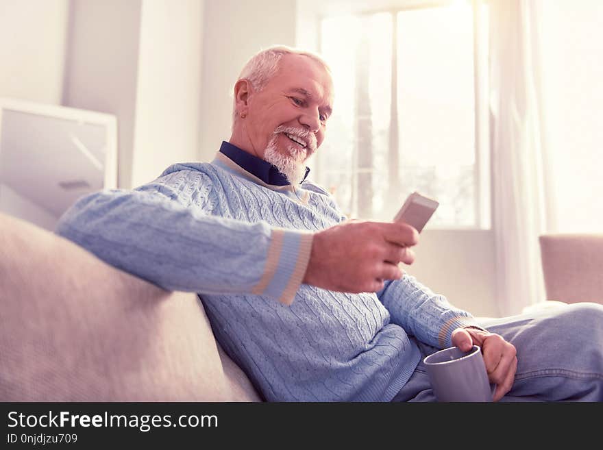 Radiant senior checking. Radiant senior checking content on his mobile phone while relaxing at home. Radiant senior checking. Radiant senior checking content on his mobile phone while relaxing at home