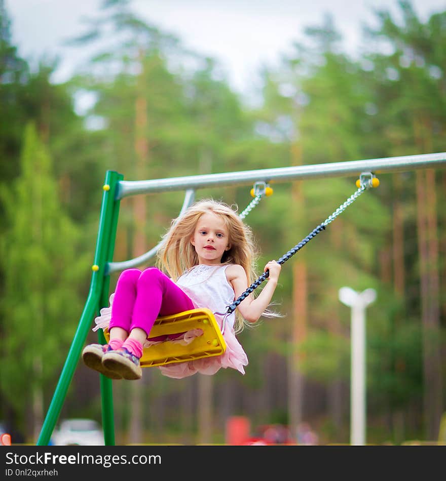 Little blonde girl smiling swinging outdoors on a playgroung