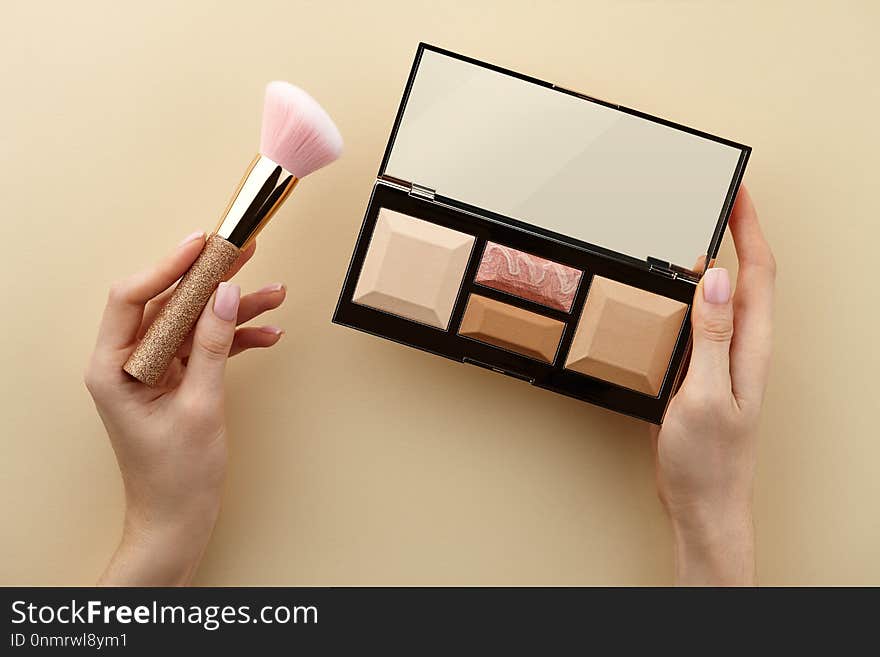 Make up artist holding sculptor palette and brush in hands on beige background, close up view. Make up artist holding sculptor palette and brush in hands on beige background, close up view