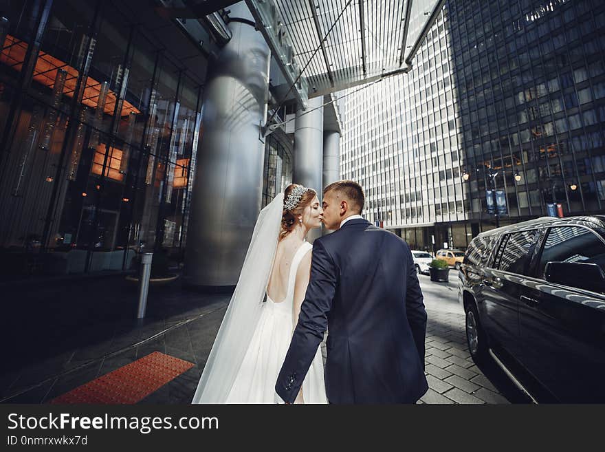 Elegant bride in a white dress and veil. Handsome groom in a blue suit. Couple in a big town. Elegant bride in a white dress and veil. Handsome groom in a blue suit. Couple in a big town