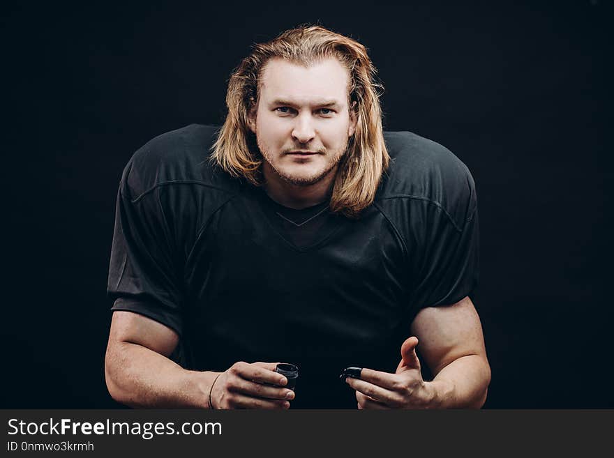 Portrait of determined American football player in black uniform with unprotected head, running with ball against black background. Portrait of determined American football player in black uniform with unprotected head, running with ball against black background