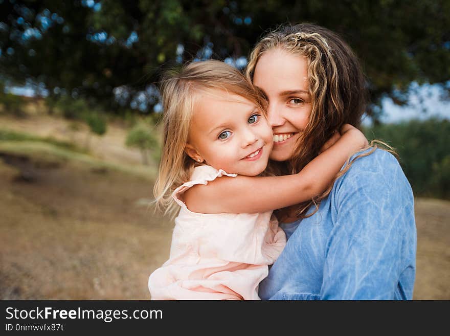 Curly blond mother with daughter walking in the field hugging and laughing. Curly blond mother with daughter walking in the field hugging and laughing.