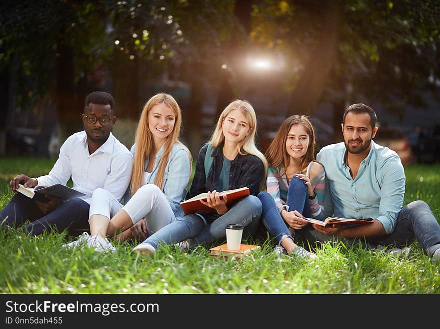 Mixed-race group of students sitting together on green lawn of university campus