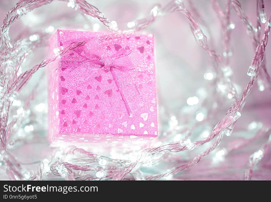 Pink gift box with a bow and small hearts on a silver blurred background. Beautiful sparkling gift for all holidays. Pink gift box with a bow and small hearts on a silver blurred background. Beautiful sparkling gift for all holidays