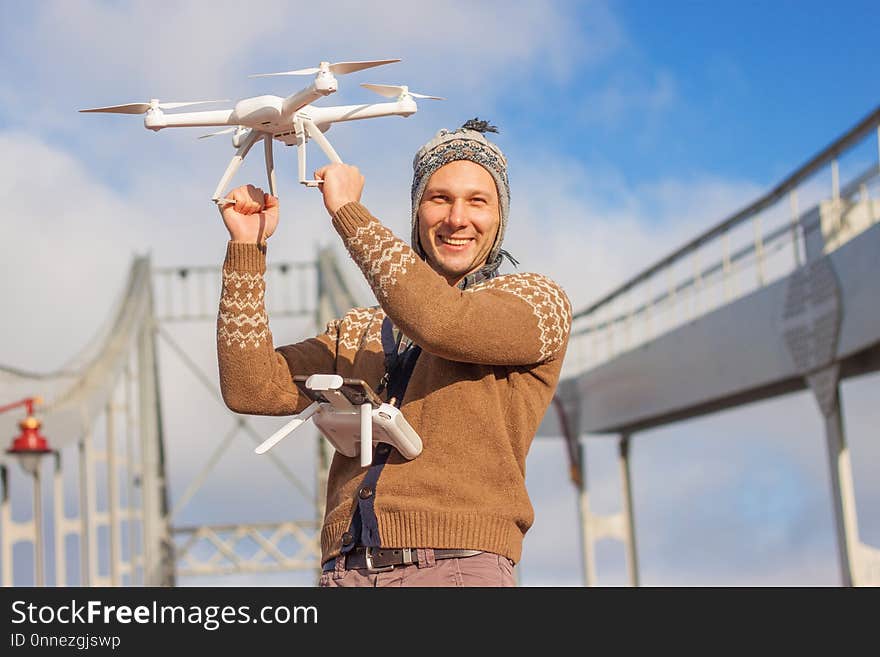 A young handsome man of European appearance launches a drone in the background of a blue sky on a bridge in winter.