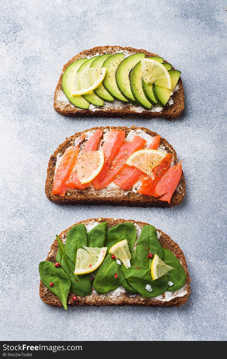 Open sandwiches with spinach and avocado salmon on a grey table.