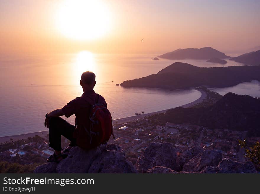 Traveler relaxes on a cliff and admires the amazing sea bay