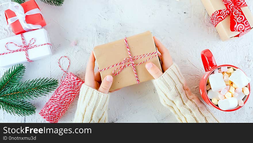 child is holding Christmas gift box tied with a red ribbon, red cup cocoa with marshmallow on the white background. Christmas card Holiday Concept, copy space. child is holding Christmas gift box tied with a red ribbon, red cup cocoa with marshmallow on the white background. Christmas card Holiday Concept, copy space