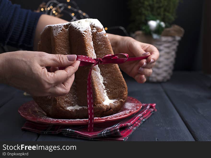 Italian Christmas cupcake with powdered sugar. Traditional festive pastries in female hands. Dark background and decor with lights. Dark photo. Free space for tex