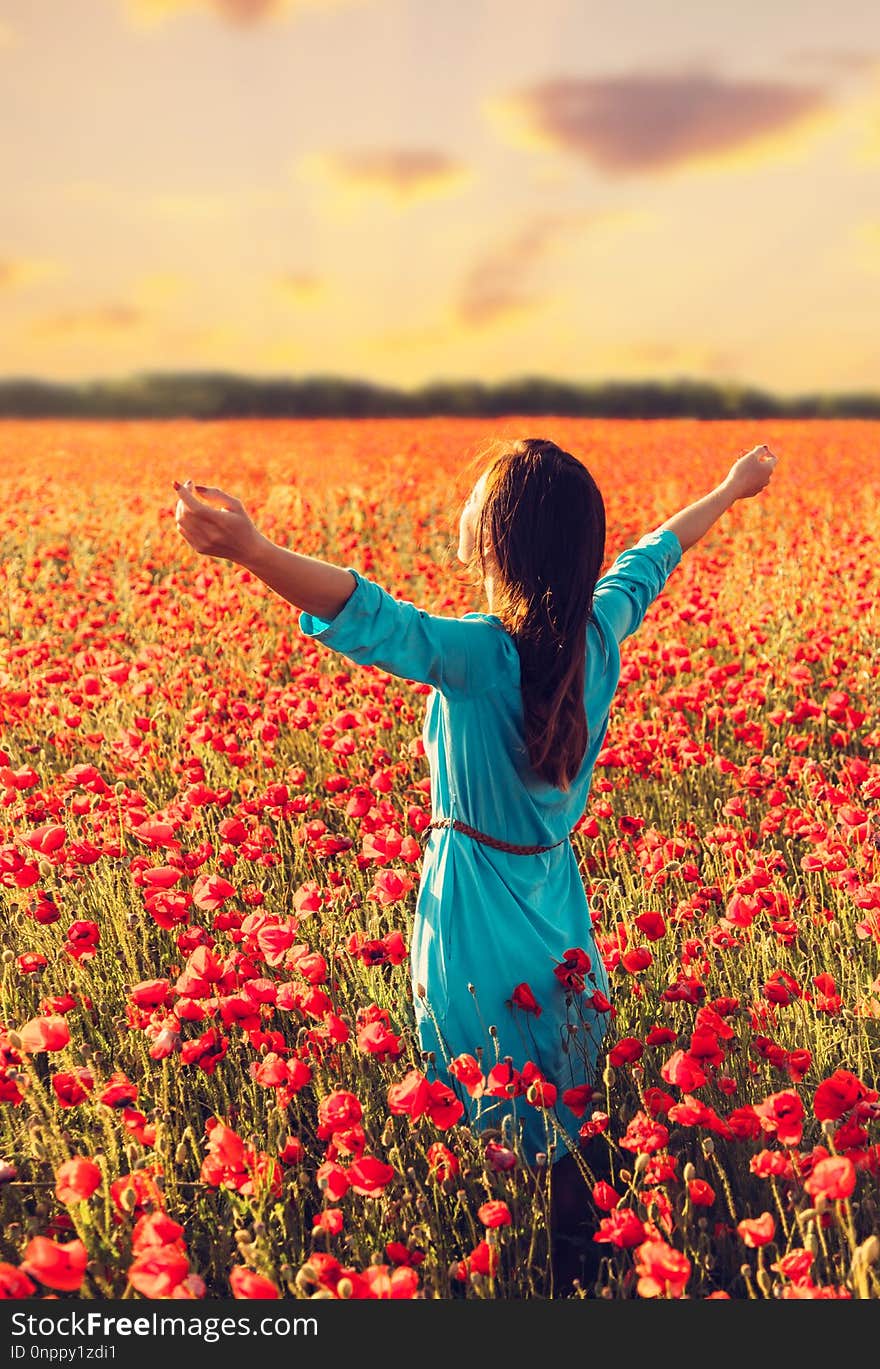 Happy young woman standing with raised arms in red poppies meadow at sunset. Happy young woman standing with raised arms in red poppies meadow at sunset.