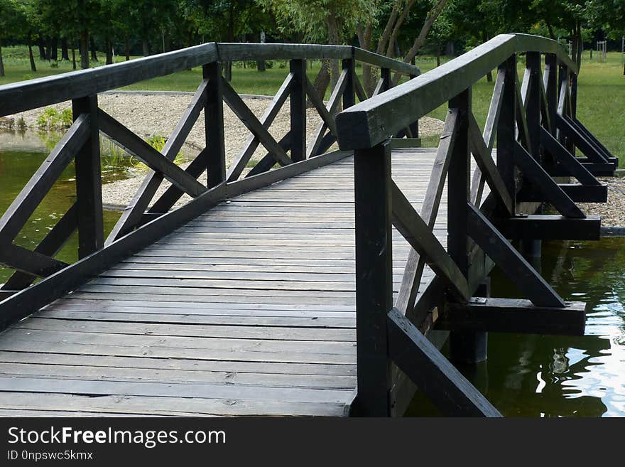 Wooden foot bridge over small pond in green public park in summer light. Wooden foot bridge over small pond in green public park in summer light