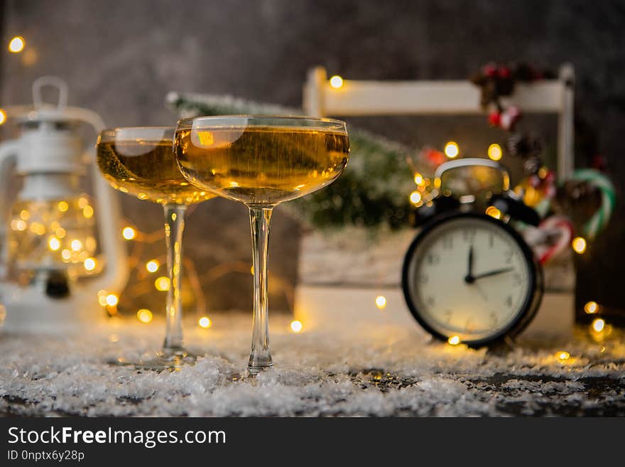 Picture of two wine glasses on table with snow on blurred background with Christmas tree, lantern, clock. Picture of two wine glasses on table with snow on blurred background with Christmas tree, lantern, clock