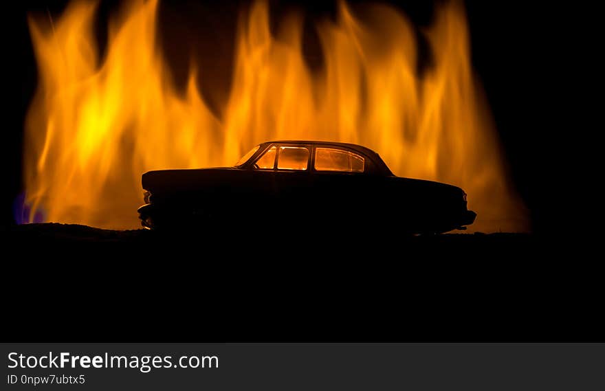 Silhouette of old vintage car in dark foggy toned background with glowing lights in low light. Selective focus